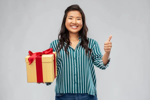 Счастливая азиатка с подарочной коробкой показывая большие пальцы вверх — стоковое фото