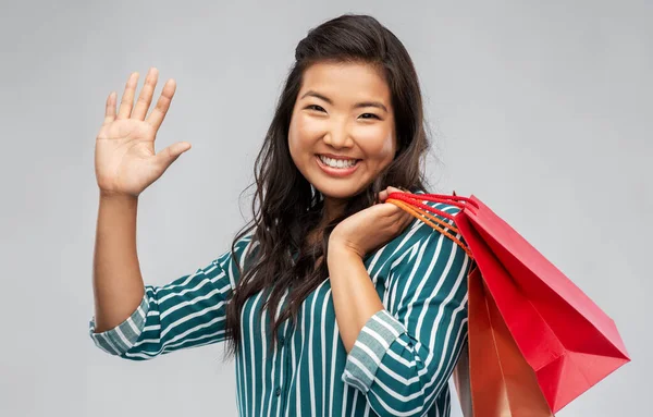 Feliz asiático mujer con compras bolsas ondeando mano — Foto de Stock