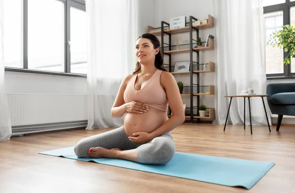 Happy pregnant woman sitting on yoga mat at home — Stock Photo, Image