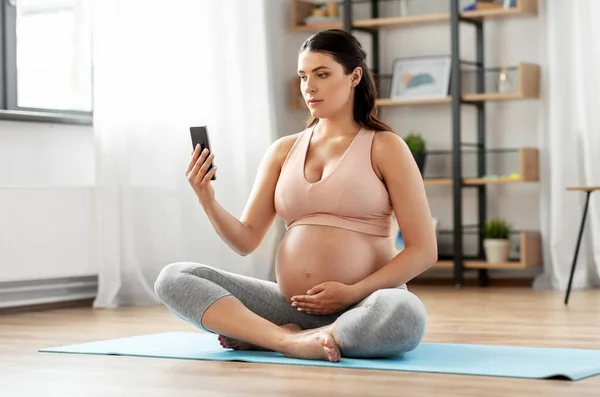 Donna incinta con smartphone che si esercita a casa — Foto Stock