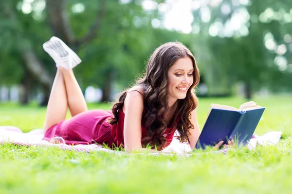 Szczęśliwa uśmiechnięta kobieta czyta książkę w letnim parku — Zdjęcie stockowe