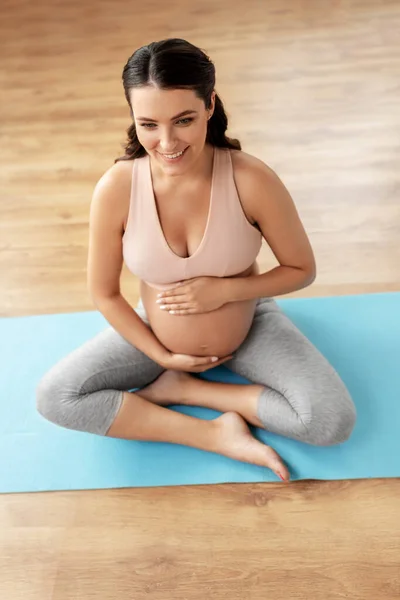 Счастливая беременная женщина сидит дома на коврике для йоги — стоковое фото