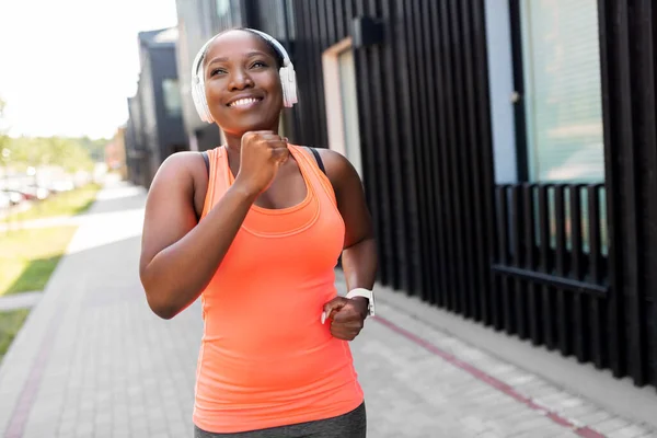 Femme africaine heureuse dans les écouteurs courir à l'extérieur — Photo