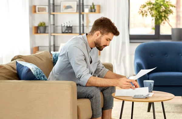 Homme avec des factures comptant sur la calculatrice à la maison — Photo