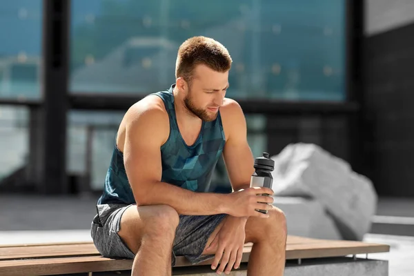 Tired sportsman with bottle sitting on city bench — Stock Photo, Image