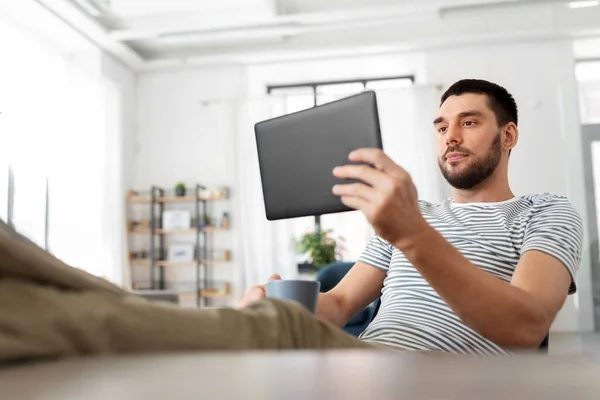 Man met tablet pc rustende voeten op tafel thuis — Stockfoto