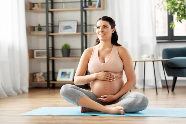 Happy pregnant woman sitting on yoga mat at home — Stock Photo, Image