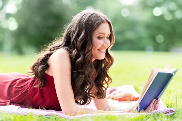 Feliz mulher sorrindo livro de leitura no parque de verão — Fotografia de Stock