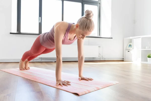 Jonge vrouw doen plank oefening op mat thuis — Stockfoto