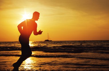 Genç, formda bir adam tropik bir plajda koşuyor.