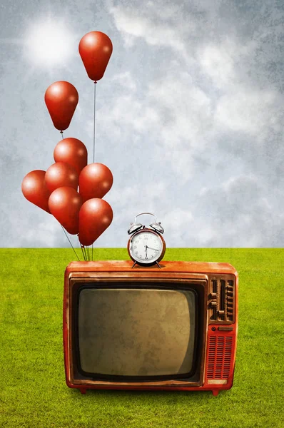 Old television with alarm clock and balloons at green field, Wat