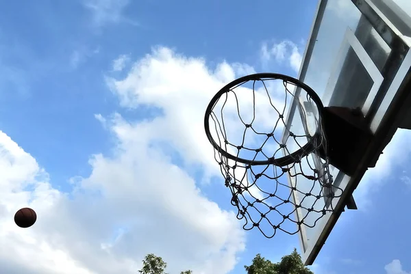 Basketbal hoepel met bal in de lucht en wolken in de blauwe lucht terug — Stockfoto