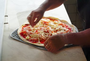 Şef pizzanın üzerine peyniri koyuyor, yakın çekim.