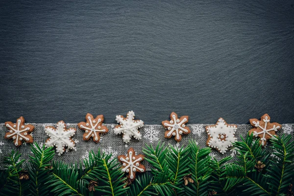 Рамка с еловыми ветками, печеньем и рождественскими украшениями на темном каменном фоне. Вид сверху . — стоковое фото