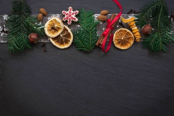 Keret, a fenyő ágak, a cookie-k és a karácsonyi díszek a sötét kő háttér. Szemközti nézet. — Stock Fotó