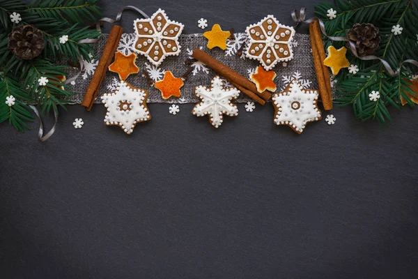 Marco con ramas de abeto, galletas y decoraciones navideñas sobre fondo de piedra oscura. Vista superior . — Foto de Stock