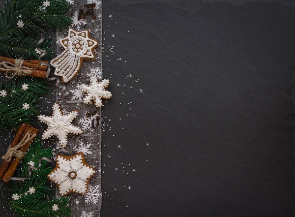 Cadre avec branches de sapin, biscuits et décorations de Noël sur fond de pierre sombre. Vue du dessus . — Photo