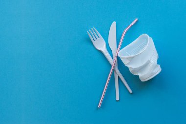 Çevre kirliliğinin bir sembolü olarak mavi bir arka plan üzerinde beyaz plastik tek sofra. Plastik bir kişilik ile hayır söylemek.