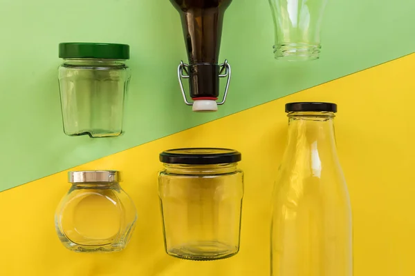 Frasco de vidrio vacío y botella sobre fondo amarillo y verde, vista desde la parte superior — Foto de Stock