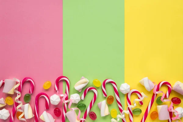 Alguns doces bengalas, marshmallows e merengues estão espalhados em papel colorido — Fotografia de Stock