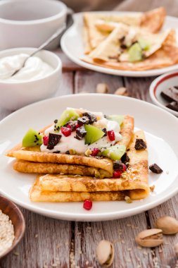 Erimiş çikolatalı ince krepler, susam tohumları, nar ve badem.