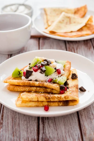 Triangle rolled pancakes with cream, pieces of chocolate, banana, kiwi and pomegranate — Stock Photo, Image