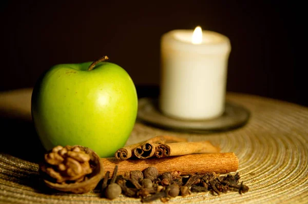 Зеленое яблоко, корица, грецкий орех и свеча на столе — стоковое фото