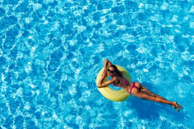 Gülümseyen güneş gözlüğü ve pembe bikini yüzme havuzu sarı şişme halkası üzerinde genç kadın