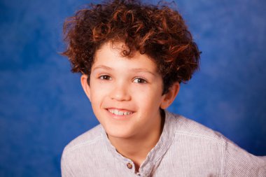 Yakın çekim kıvırcık saçlı ve kahverengi gözleri mavi arka plan karşı gülümseyen varoluş çocuk portresi