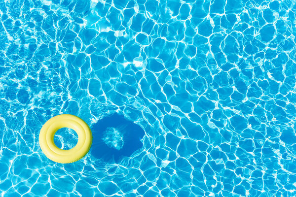 Top view picture of empty yellow rubber ring floating on blue water surface with copy-space