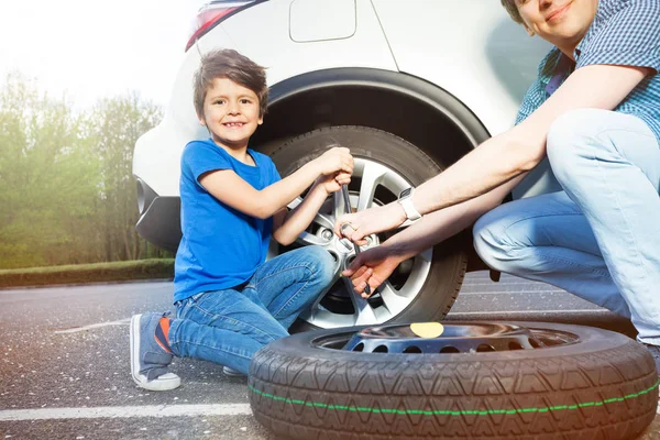 晴れた日に外に車のホイールを変更する彼の父を助けること幸せな男の子の肖像画 — ストック写真