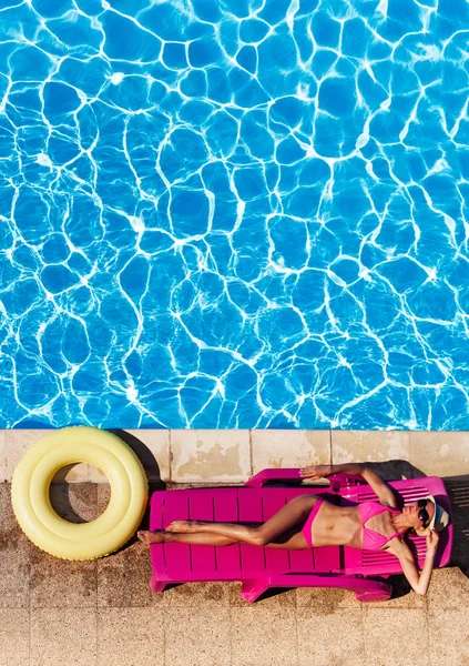 美丽的年轻女子在比基尼上躺在粉红色的日光浴在池边鸟瞰 — 图库照片