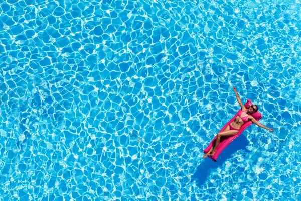 在游泳池充气床垫上躺在粉红色比基尼的苗条女人的鸟瞰图 — 图库照片