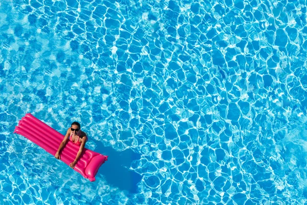 在太阳镜下观看的年轻女子在粉红色充气床垫上游泳和看相机 — 图库照片