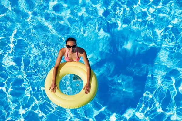 阳光明媚的日子 太阳镜中的年轻女子在泳池里游泳 戴着黄色橡胶戒指 — 图库照片