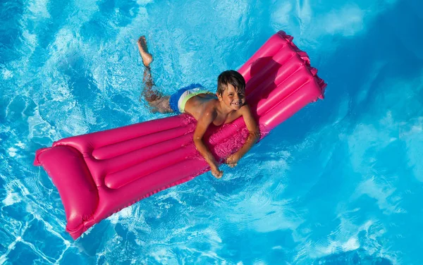 幸せな 歳男の子水泳プールでピンクの膨脹可能なマットレスに上からの眺め — ストック写真