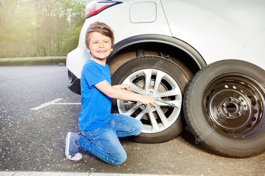 Portrait of happy little boy changing tyre of car using lug wrench
