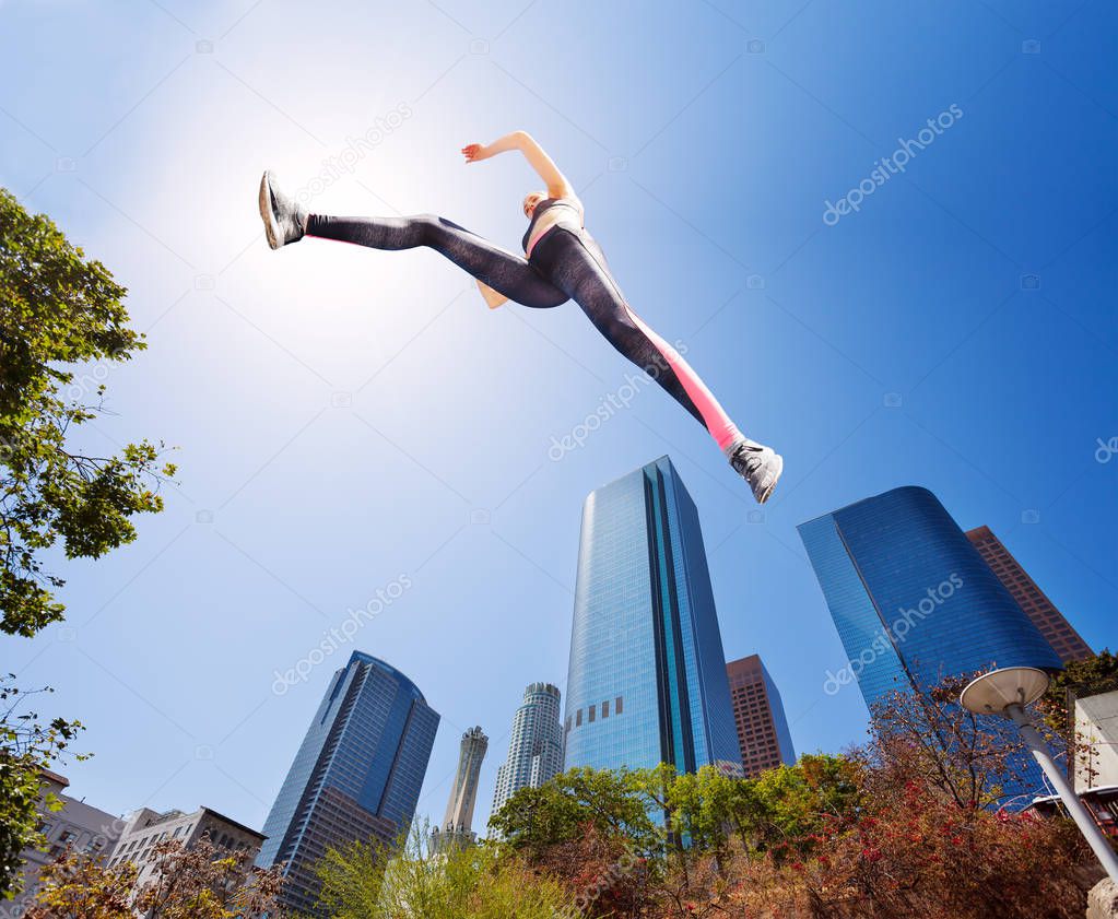 Young sportswoman captured in long jump in summer park in downtown view from below