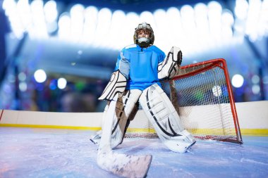 Low-angle portrait of young goaltender preparing to catch the puck during hockey game at ice arena clipart
