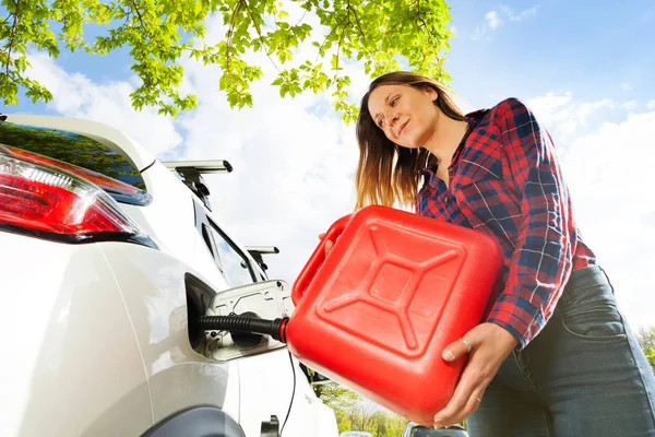 赤缶から彼女の車のガソリン タンクに美しい若い女性の注ぐ燃料のローアングル ショット — ストック写真