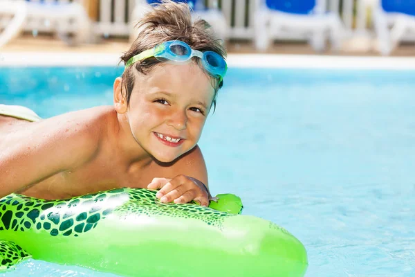 Close-up portrait of happy boy in goggles swimming with inflatable toy in the pool