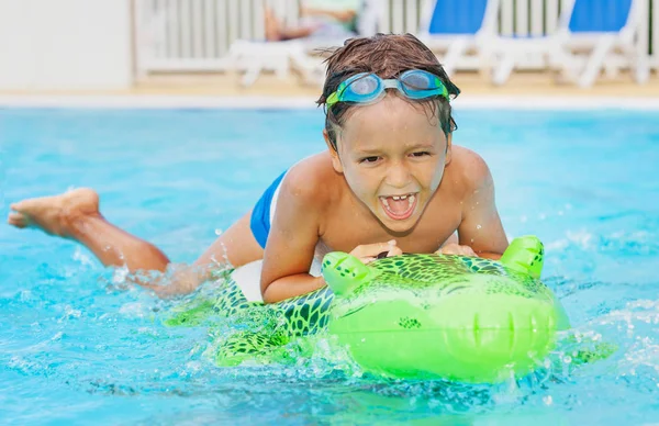 スイミング プールで大きな緑の膨脹可能なおもちゃを楽しんで少年の肖像画 — ストック写真