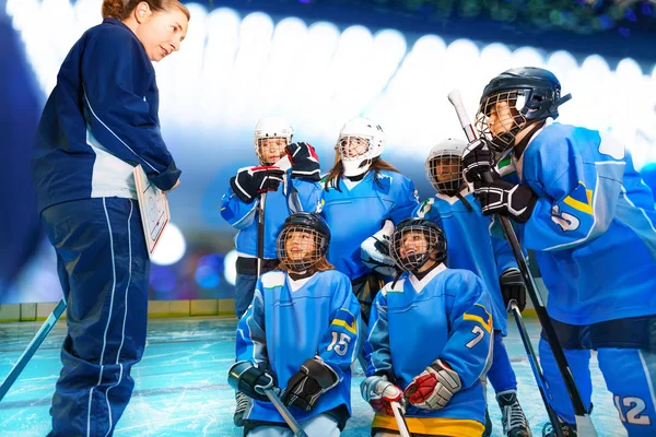 Female coach and hockey team discussing game plan during time out on ice rink