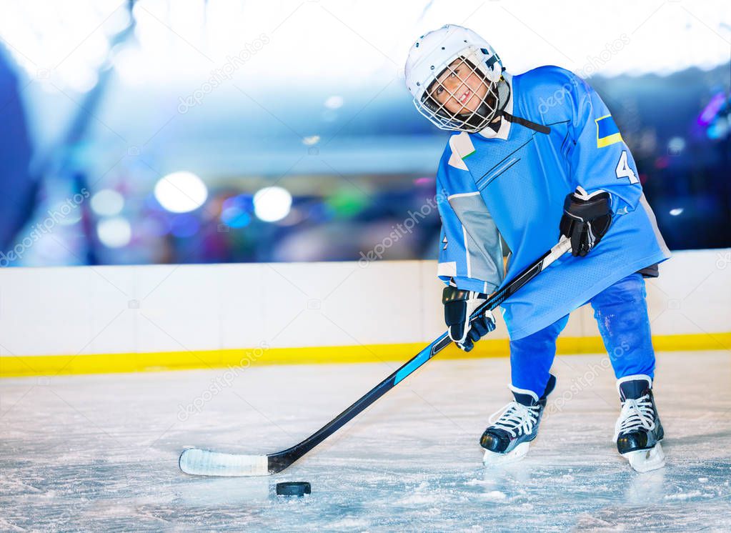 Portrait of happy boy, little hockey player, standing on ice rink and passing the puck