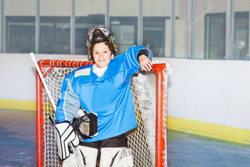 Portrait of teenage boy goaltender, standing next to the net after hockey match smiling