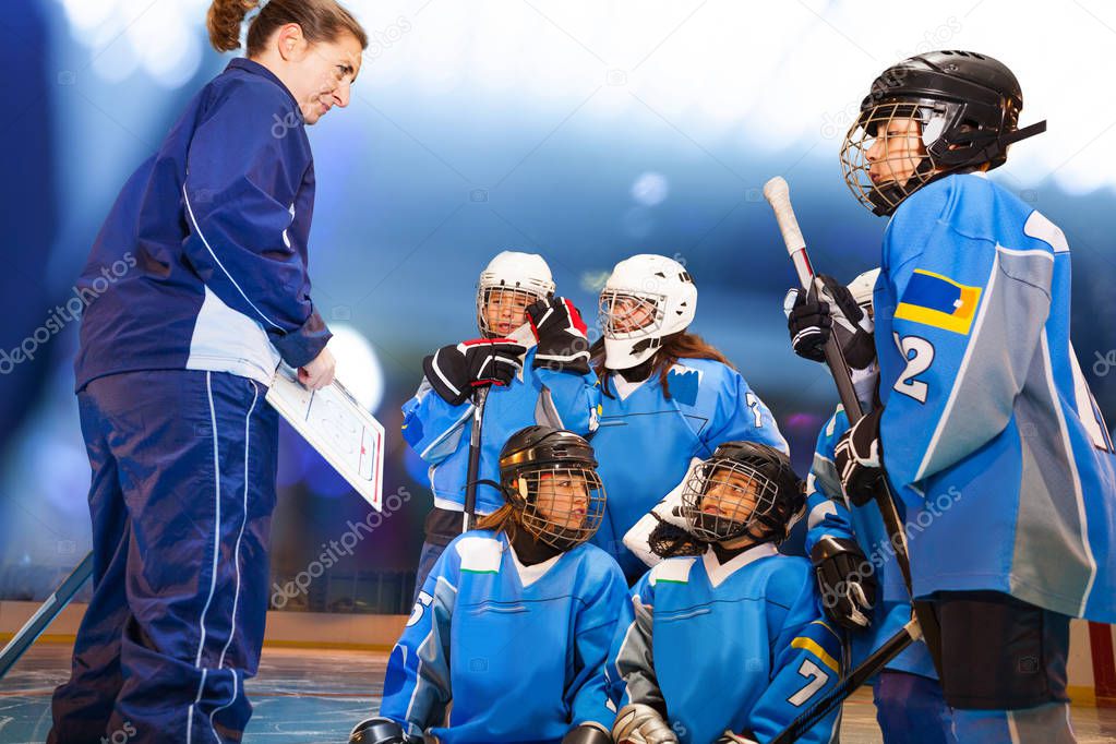 Cheerful female coach showing clipboard with game plan to ice hockey team