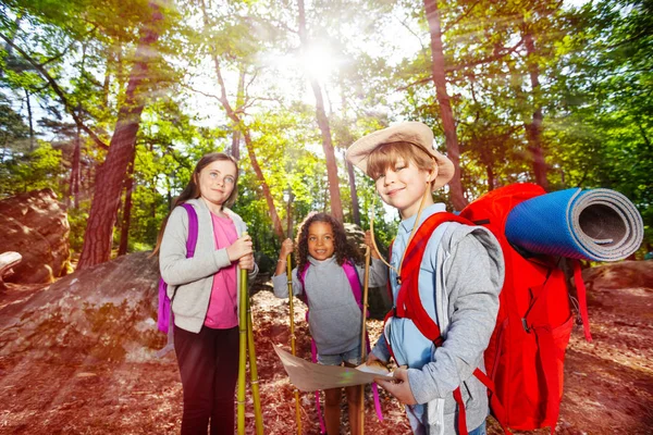 Group of kids in the forest with hiking poles map and backpack