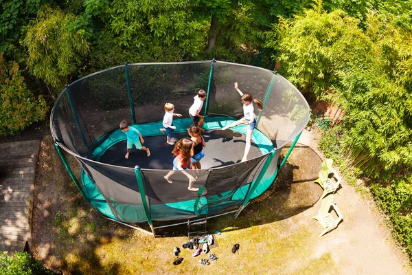 High angle shot of age-diverse boys and girls jumping on the trampoline with enclosure in the garden — Stock Image High Angle Shot Age Diverse Boys Girls Jumping Trampoline Enclosure Royalty Free Stock Photos