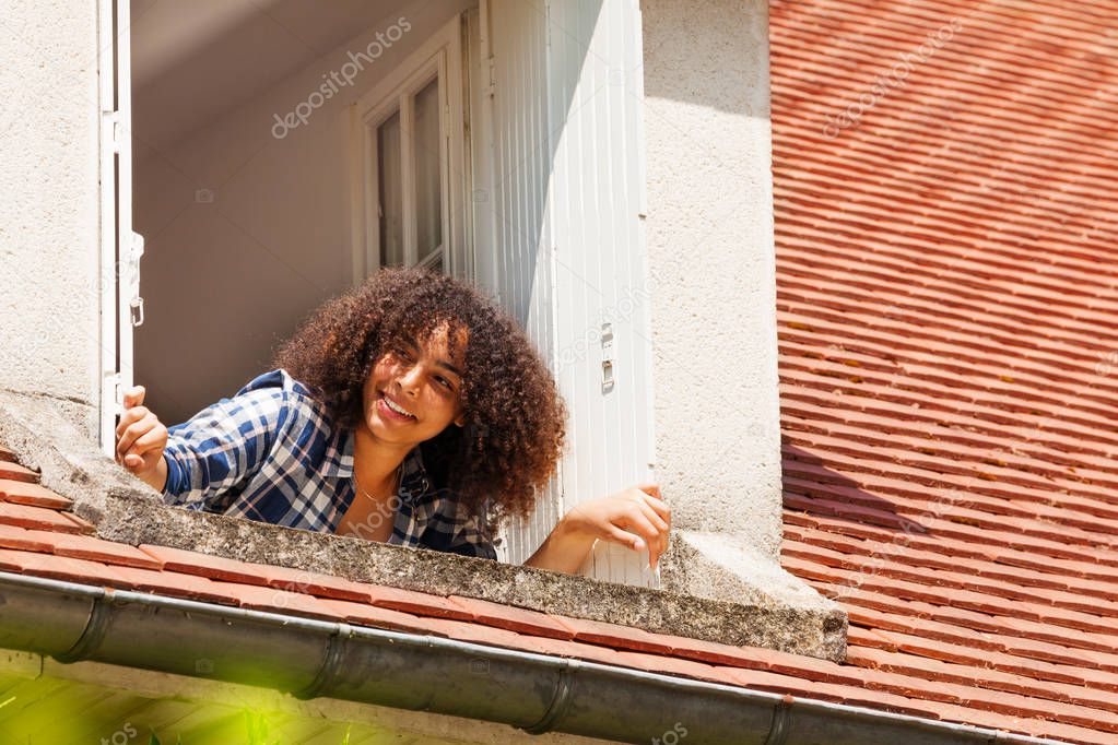 Portrait of beautiful African girl teenager opening shutters and looking out the attic window