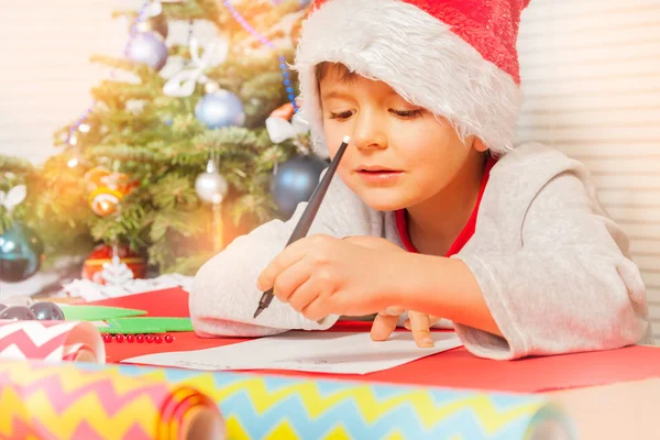 特写肖像的小男孩坐在圣诞树旁边 写信给圣诞老人 — 图库照片